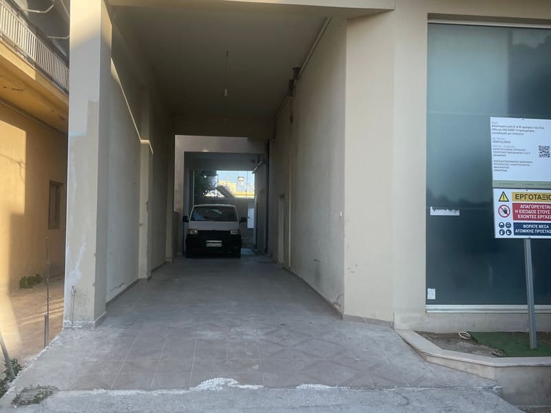 Καλυμμένη είσοδος/διάδρομος πρόσβασης προς το κτίριο, με πινακίδα εργοταξίου ακόμα αναρτημένη