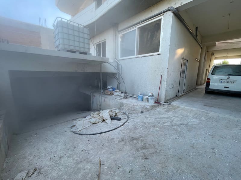 Η εξωτερική όψη του ημιυπόγειου επιπέδου, με παράθυρα, δεξαμενή νερού και υλικά κατασκευής στην αυλή